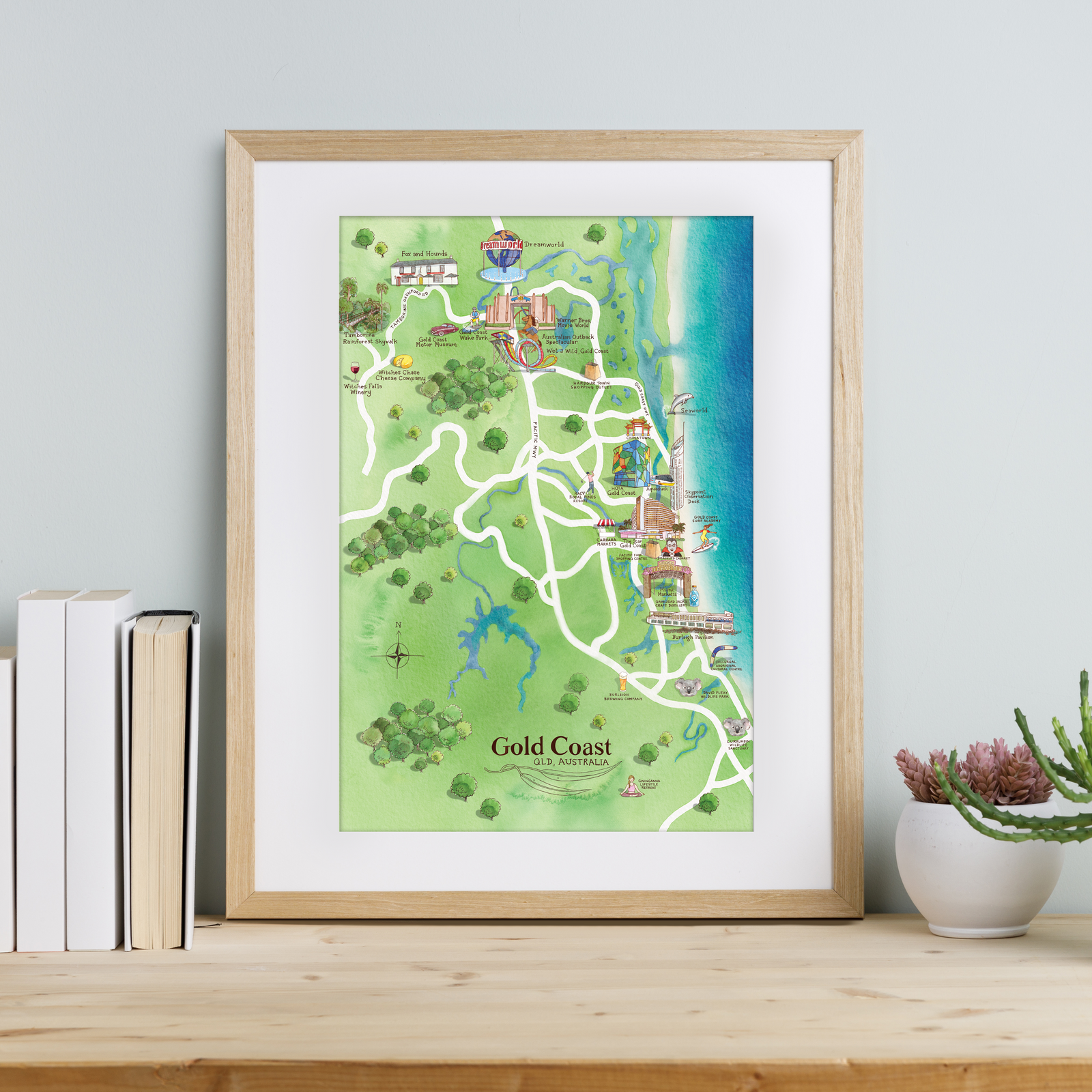 Framed map of Gold Coast on a wooden surface with books and a plant.